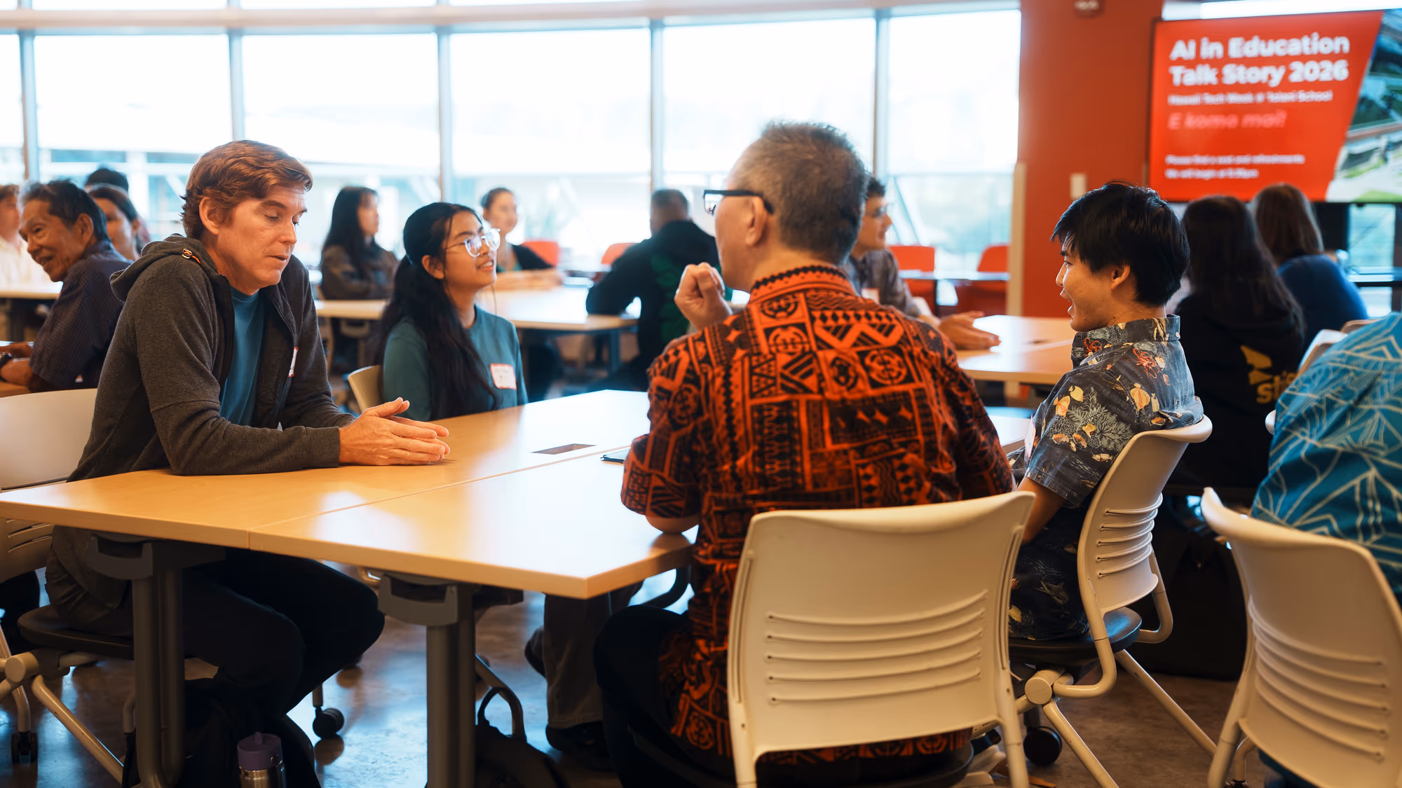 Participants talk around a table beside an AI in Education Talk Story 2026 sign.