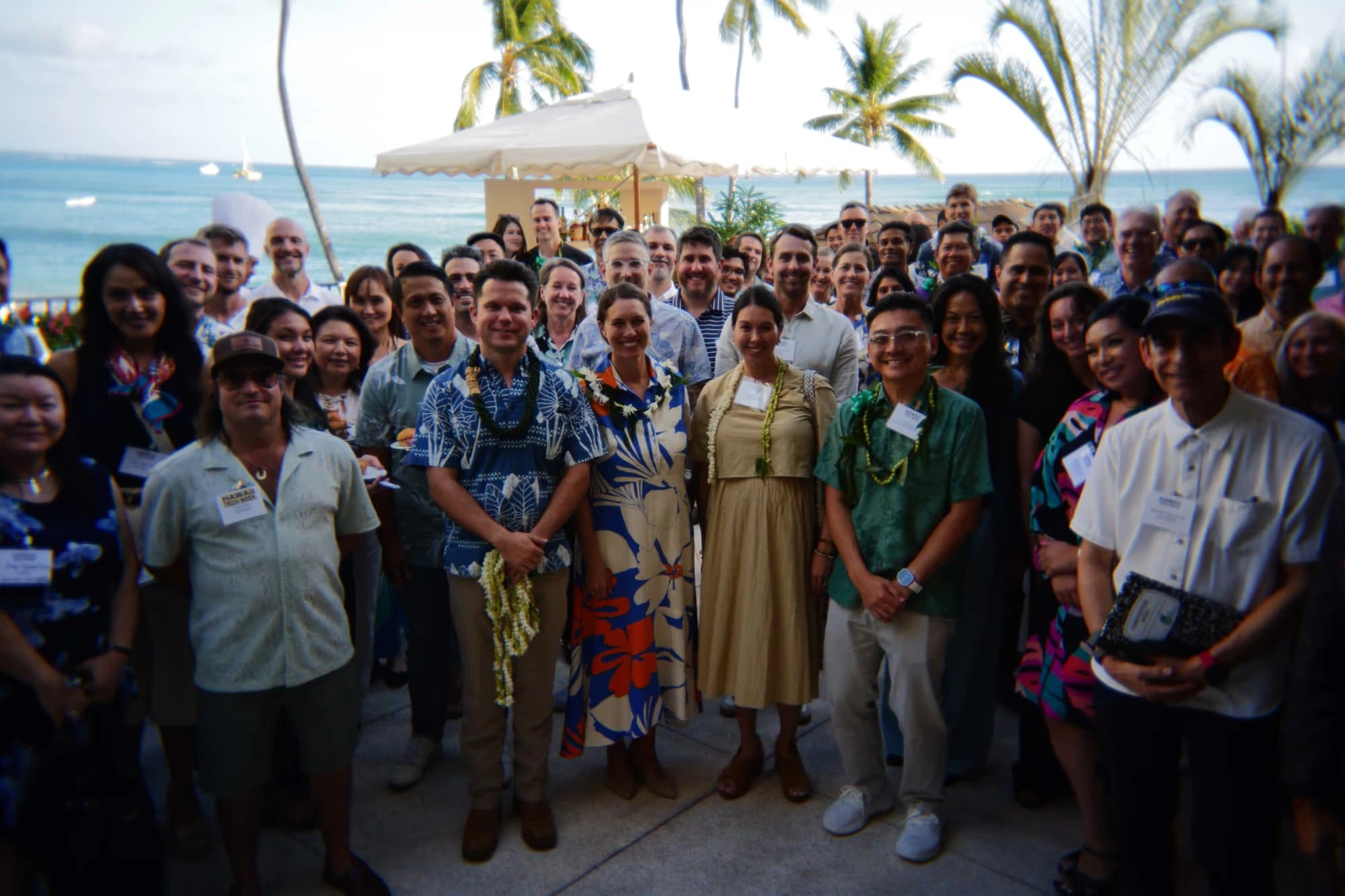 A group gathered outdoors at the Executive Forum, with palms and the ocean behind them.