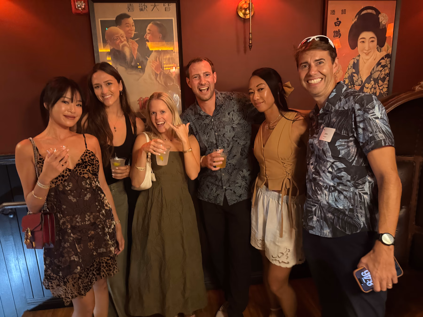 Six guests smile and pose together against the warm red walls at the Official Mixer.