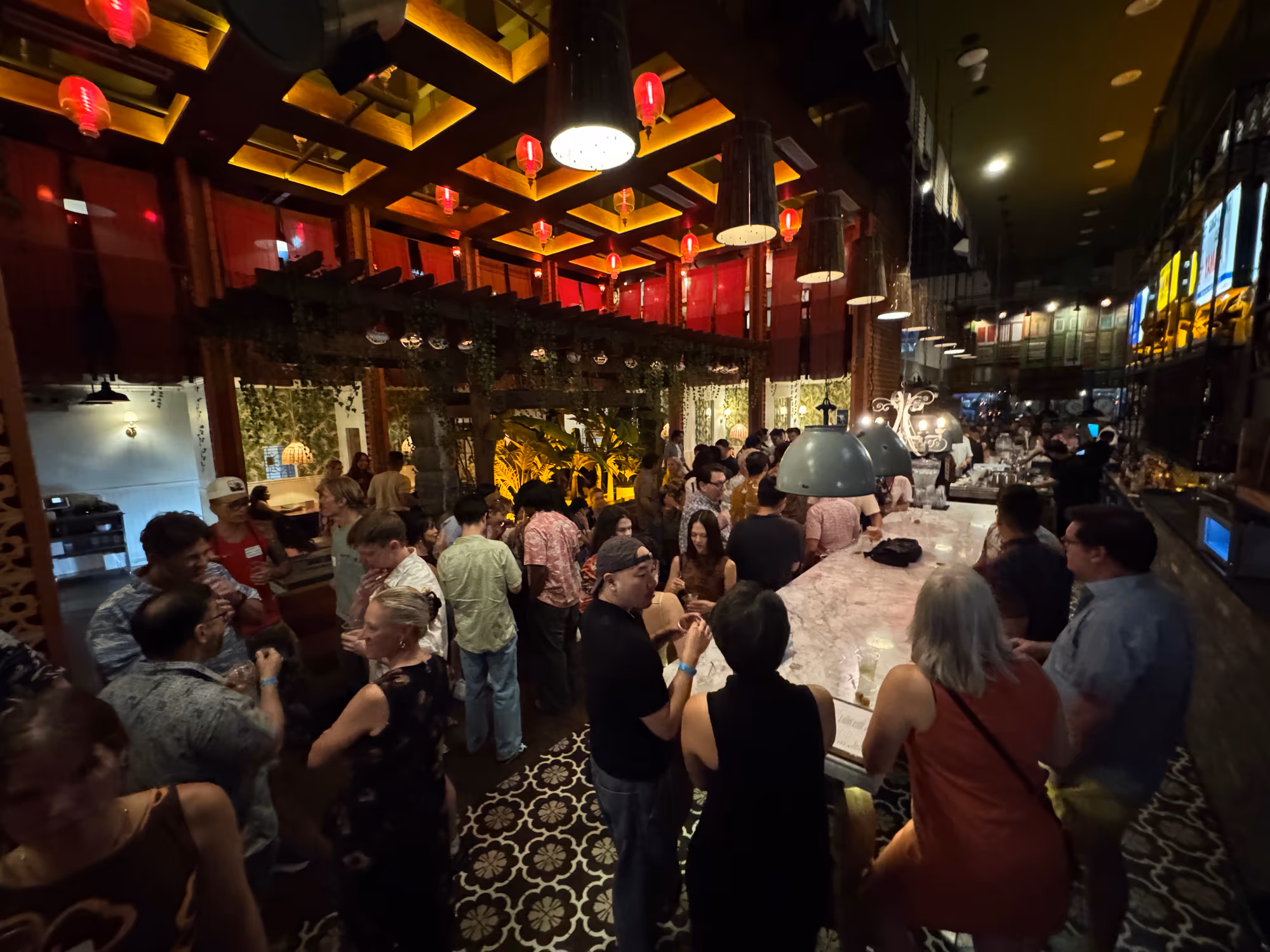 Participants talk in small groups around the long bar beneath warm lights at the HTW Official Mixer.