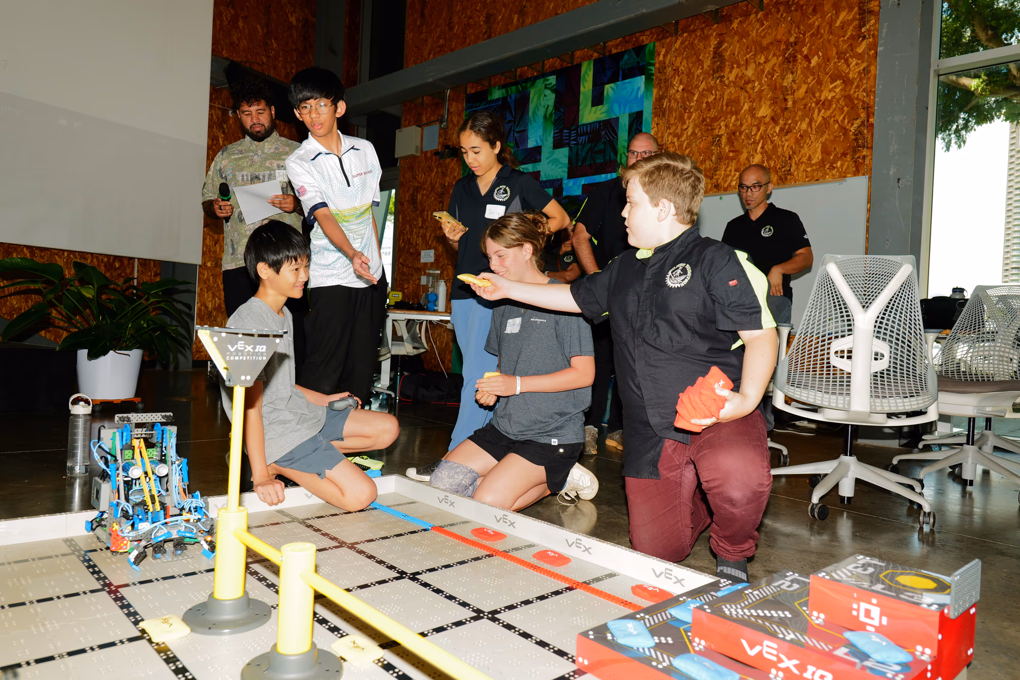 Young participants and adults gather around a robotics demonstration table.