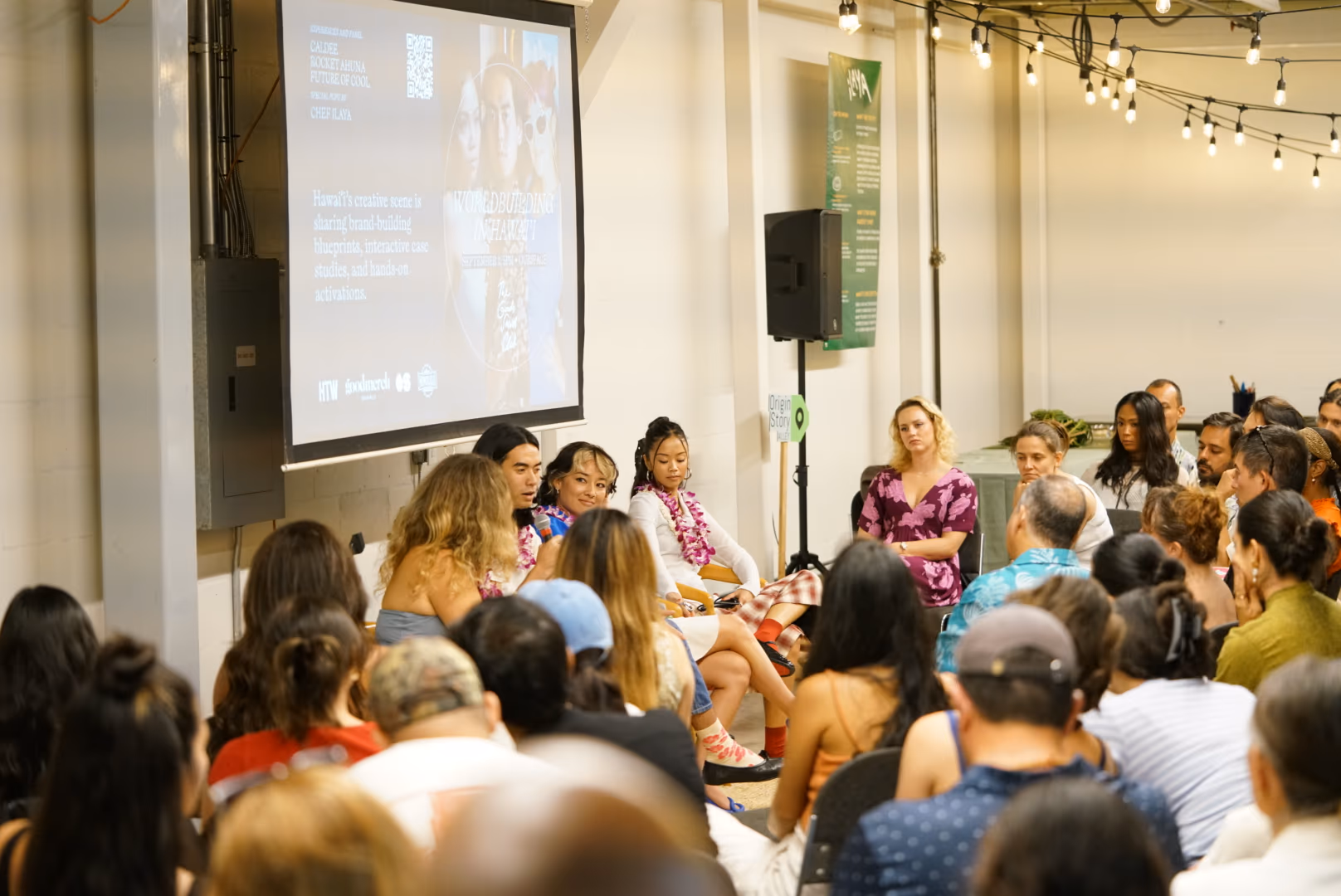 An audience gathers around a seated conversation beside a Worldbuilding in Hawaii presentation.
