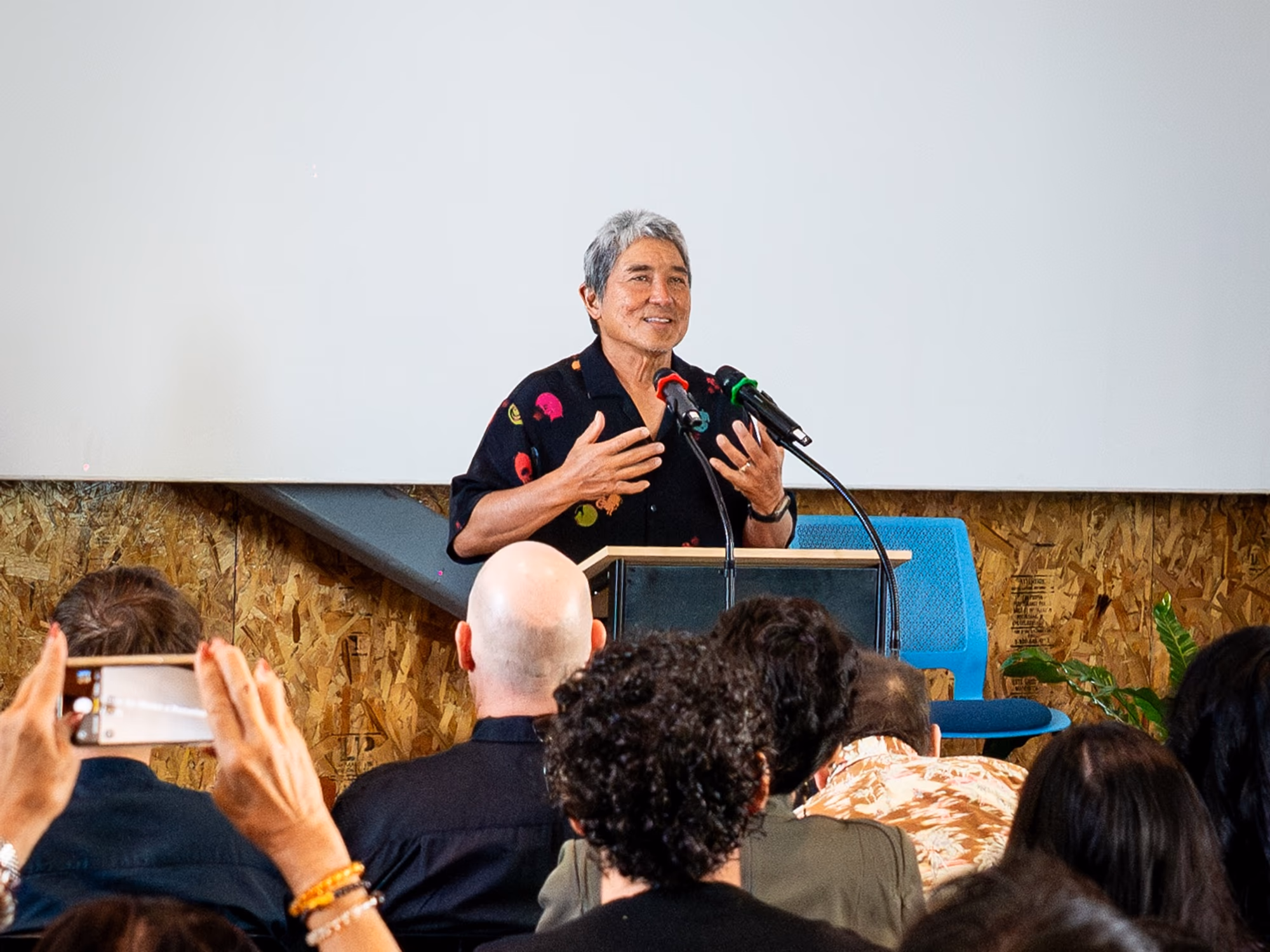Keynote speaker at podium with audience filming the talk